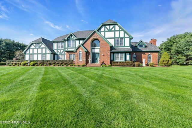 tudor-style house with a chimney, brick siding, and a front yard