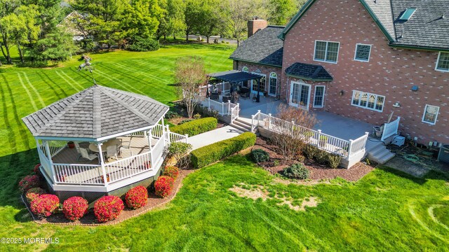 back of property featuring a gazebo, brick siding, a deck, a chimney, and a yard