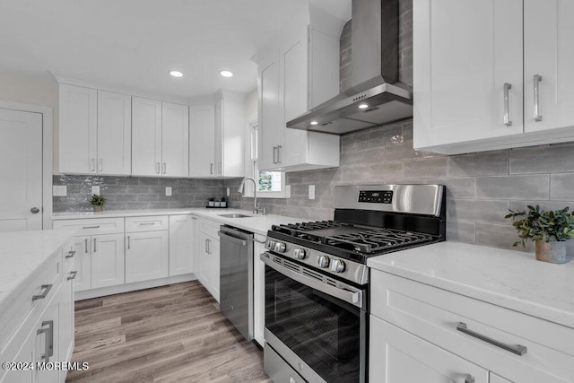 kitchen featuring recessed lighting, a sink, wall chimney exhaust hood, white cabinets, and appliances with stainless steel finishes