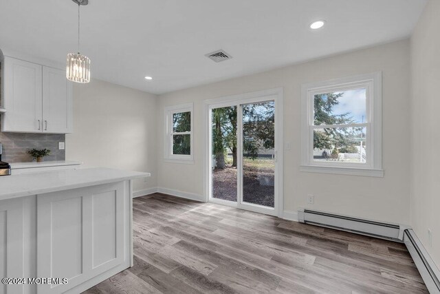 unfurnished dining area featuring a baseboard heating unit, baseboards, light wood-style flooring, and visible vents