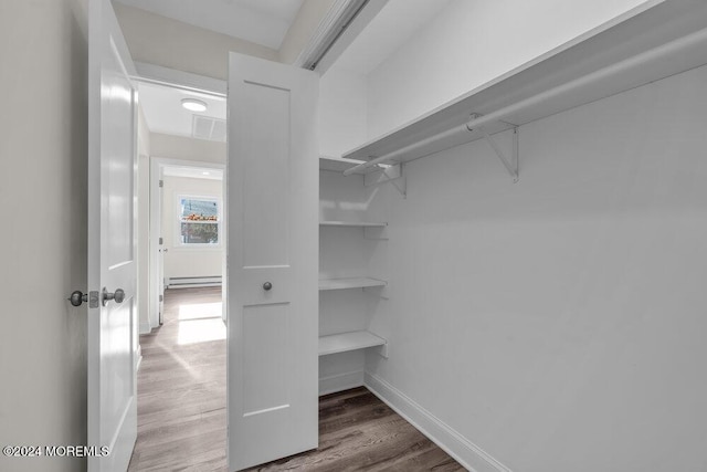 spacious closet with wood finished floors and a baseboard heating unit