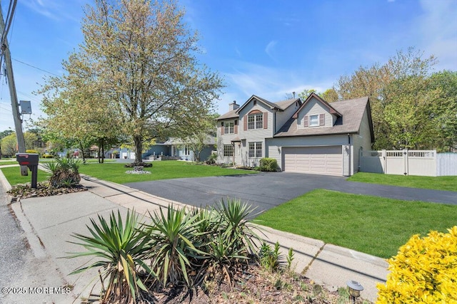 view of front facade with fence, an attached garage, a front lawn, and aphalt driveway