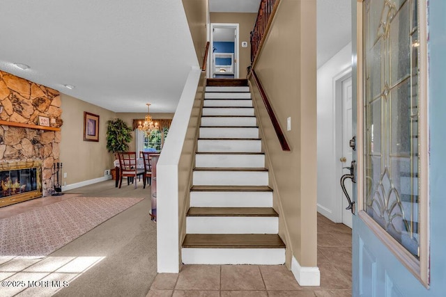 staircase with baseboards, a stone fireplace, and a chandelier
