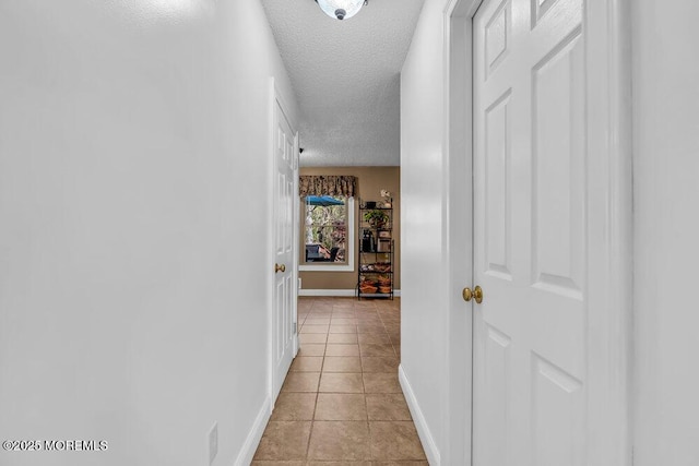 corridor featuring baseboards, a textured ceiling, and light tile patterned flooring
