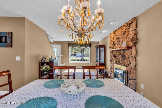 dining area with an inviting chandelier, carpet floors, a stone fireplace, and a textured ceiling
