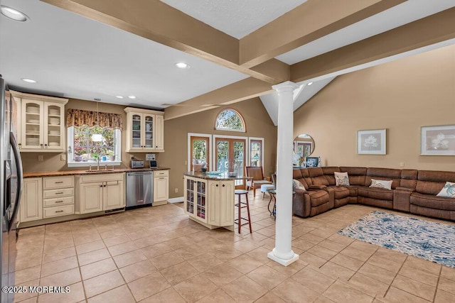 kitchen with a kitchen bar, a sink, open floor plan, stainless steel appliances, and cream cabinetry