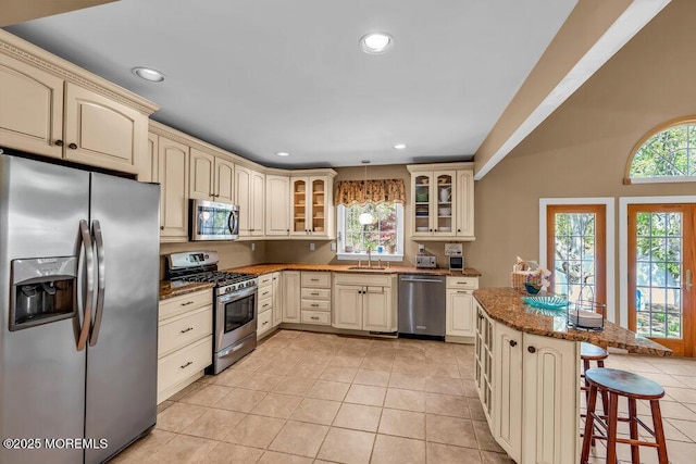 kitchen featuring appliances with stainless steel finishes, a breakfast bar area, cream cabinets, and glass insert cabinets