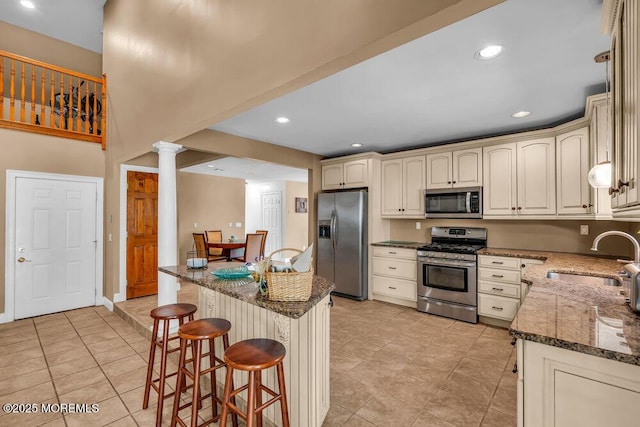 kitchen featuring a sink, appliances with stainless steel finishes, a breakfast bar, and dark stone counters