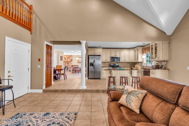 living room featuring baseboards, high vaulted ceiling, decorative columns, and light tile patterned floors
