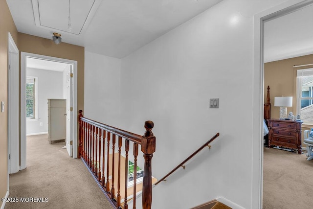 corridor featuring light colored carpet, attic access, baseboards, and an upstairs landing