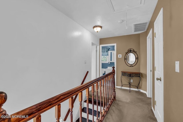 hallway featuring attic access, visible vents, baseboards, an upstairs landing, and carpet flooring