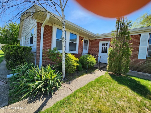 doorway to property featuring a lawn and brick siding