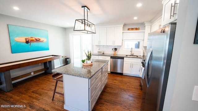kitchen with appliances with stainless steel finishes, a sink, dark wood finished floors, dark stone counters, and white cabinetry