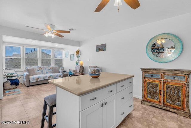 kitchen with ceiling fan, a breakfast bar area, white cabinetry, and visible vents