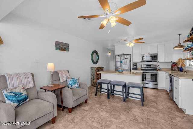 interior space with a sink, a kitchen breakfast bar, stainless steel appliances, a ceiling fan, and white cabinetry