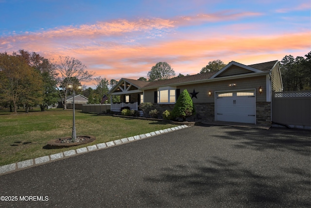 view of front facade featuring aphalt driveway, a lawn, fence, stone siding, and an attached garage