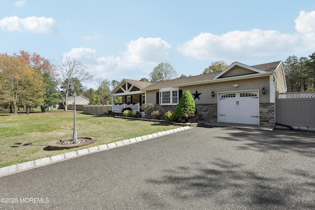 view of front of property featuring fence, stone siding, a garage, a front yard, and driveway