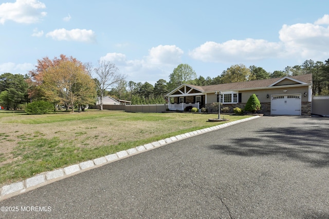 ranch-style house featuring fence, stone siding, a garage, a front yard, and gravel driveway