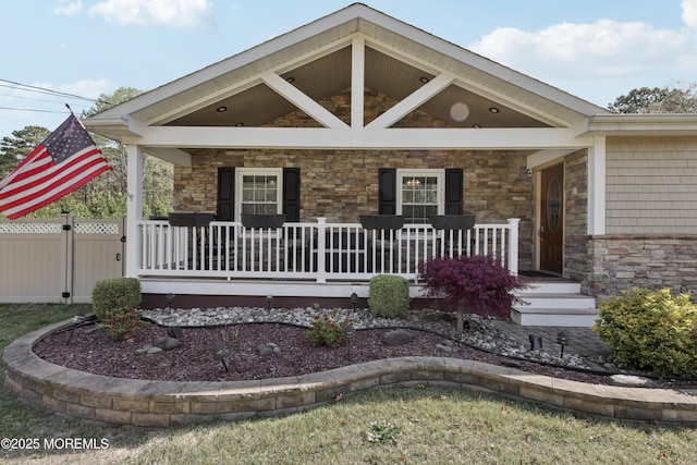 view of front facade featuring covered porch, fence, and stone siding