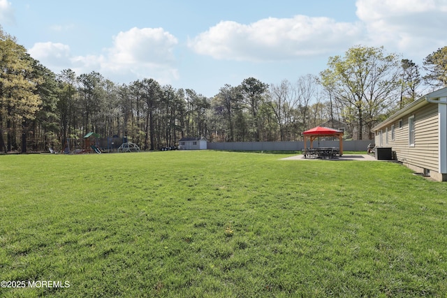 view of yard featuring a storage shed, a gazebo, fence, cooling unit, and a playground