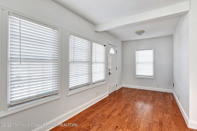 foyer entrance featuring baseboards, beamed ceiling, and wood finished floors