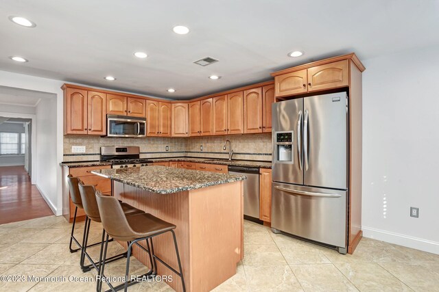 kitchen with a kitchen island, baseboards, dark stone counters, a sink, and stainless steel appliances