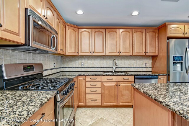 kitchen with appliances with stainless steel finishes, a sink, and dark stone countertops