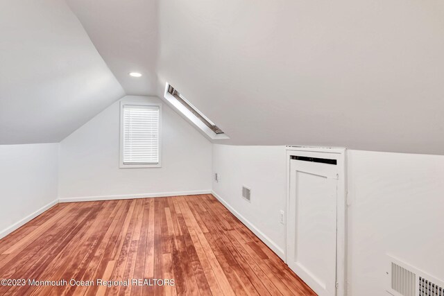 bonus room featuring visible vents, light wood-style flooring, baseboards, and vaulted ceiling with skylight