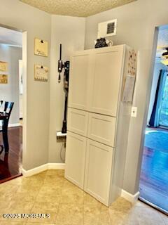 hallway featuring light tile patterned floors, baseboards, a textured ceiling, and visible vents