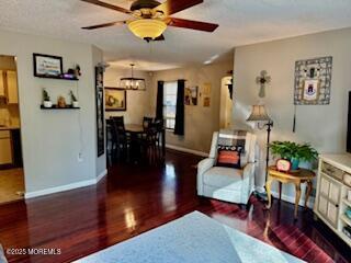 living area featuring baseboards, ceiling fan with notable chandelier, and wood finished floors