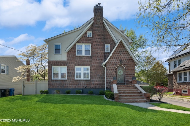 tudor house with fence, a front lawn, a chimney, and brick siding
