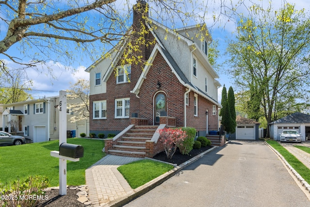 tudor-style house with a chimney, brick siding, an outdoor structure, a garage, and stucco siding