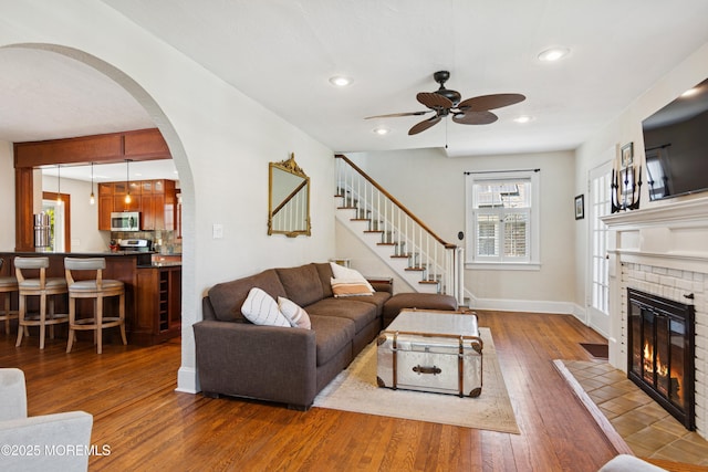 living room with ceiling fan, wood-type flooring, arched walkways, and a healthy amount of sunlight