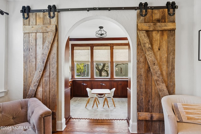 interior space with arched walkways, baseboards, a barn door, and wood finished floors