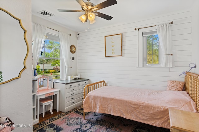 bedroom with a ceiling fan, wood walls, visible vents, and wood finished floors