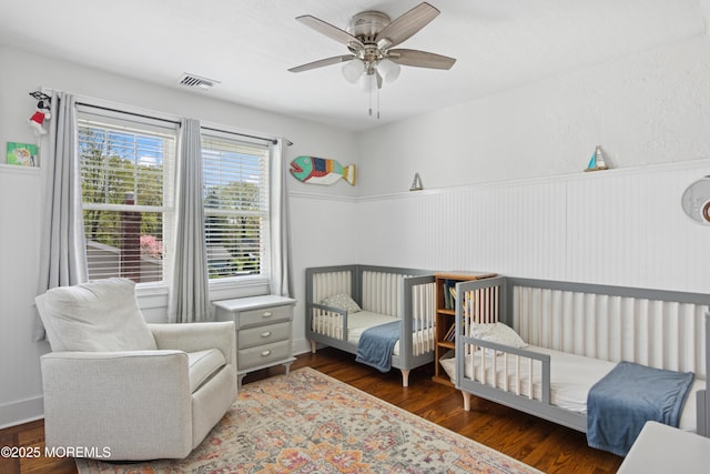 bedroom featuring a ceiling fan, visible vents, a wainscoted wall, and wood finished floors