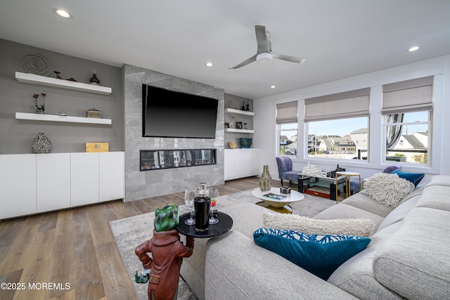 living room featuring a ceiling fan, wood finished floors, a wealth of natural light, and a tile fireplace