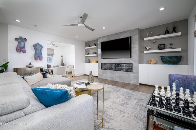 living room with ceiling fan, built in features, a fireplace, wood finished floors, and recessed lighting