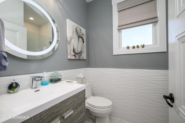 bathroom with vanity, marble finish floor, toilet, tile walls, and a wainscoted wall