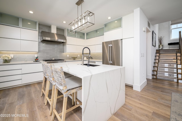 kitchen featuring modern cabinets, wall chimney exhaust hood, a sink, backsplash, and stainless steel appliances