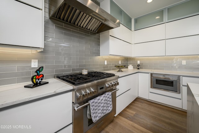 kitchen with appliances with stainless steel finishes, exhaust hood, light stone countertops, and tasteful backsplash
