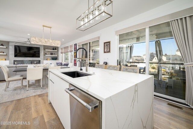 kitchen with stainless steel dishwasher, visible vents, a center island with sink, a sink, and hanging light fixtures