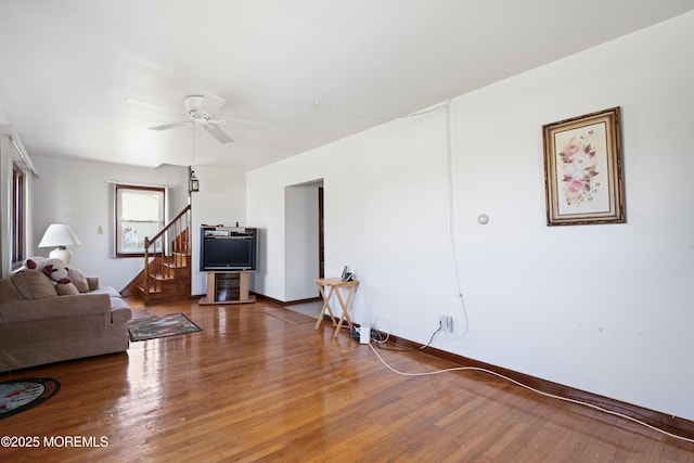 living area featuring stairs, ceiling fan, baseboards, and wood finished floors
