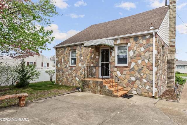 view of front of property with fence, a shingled roof, stone siding, a chimney, and a patio