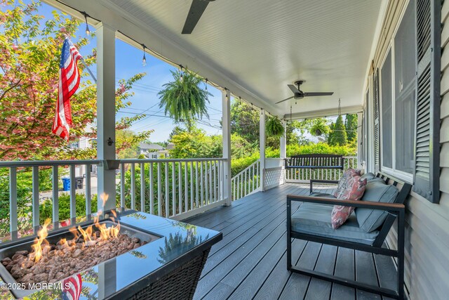 wooden terrace featuring ceiling fan, a fire pit, and covered porch