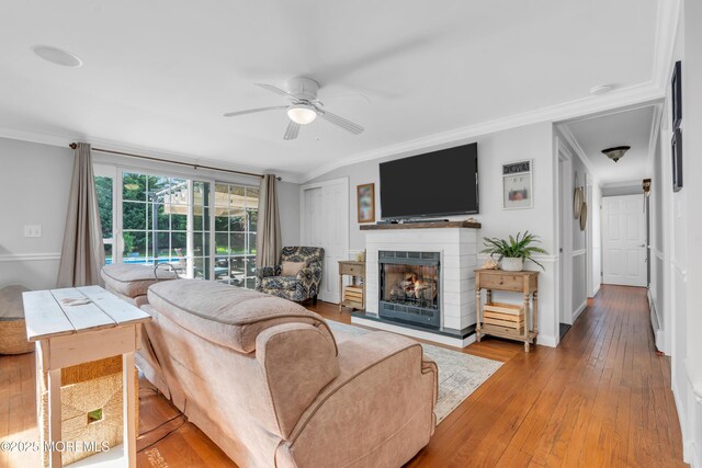 living room featuring ornamental molding, a lit fireplace, a ceiling fan, and hardwood / wood-style flooring