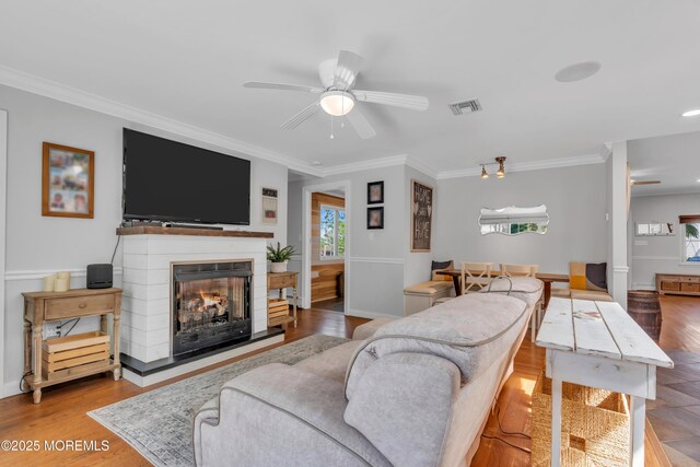 living room with a multi sided fireplace, ceiling fan, visible vents, and ornamental molding