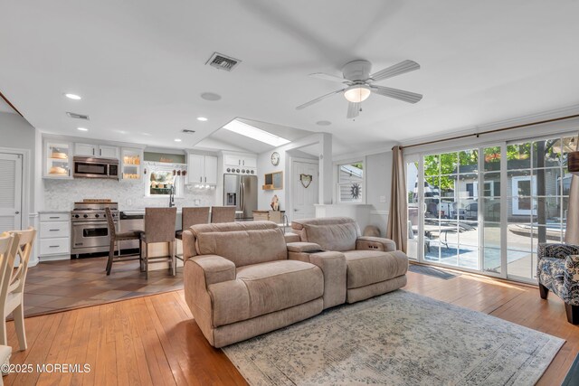 living area with a ceiling fan, lofted ceiling with skylight, light wood-style flooring, and visible vents