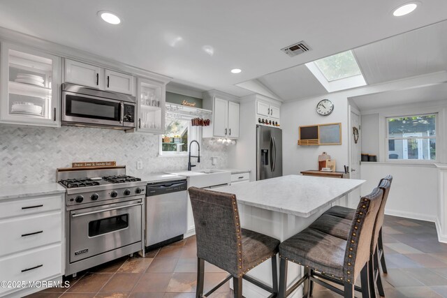 kitchen featuring white cabinets, a breakfast bar, a sink, stainless steel appliances, and visible vents