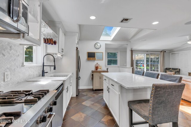 kitchen with a breakfast bar area, a skylight, appliances with stainless steel finishes, tasteful backsplash, and white cabinets
